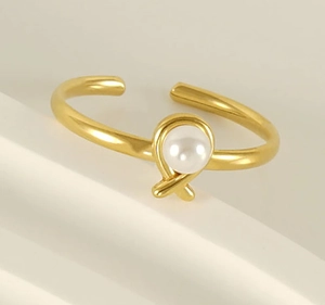 Detailed close-up of a golden open ring featuring a white pearl on a minimal background
