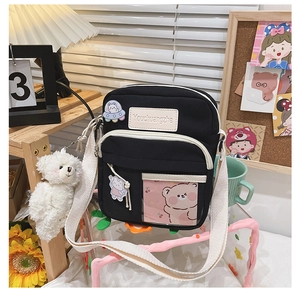 Détails d'un sac bandoulière en toile noire avec badges décoratifs et sangle blanche