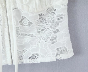 Détail de haut en dentelle blanche montrant les motifs floraux et la texture du tissu