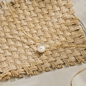 Detail of a gold stainless steel necklace featuring a round pearl and zircon on woven mat