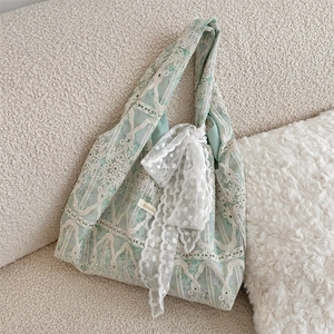 Detail of white lace mesh fabric with floral embroidery and bow on green shoulder bag