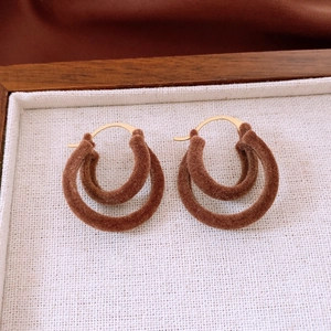 Detailed macro view of brown flocked double-hoop earrings with gold metal clasp on a tray