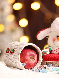 Nahaufnahme der gestrickten Weihnachts-Apfeltasche mit Knöpfen und festlichem Hintergrund