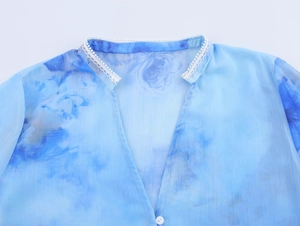 Dettaglio dello scollo a V con bordo in pizzo bianco e stampa acquerello blu su chiffon