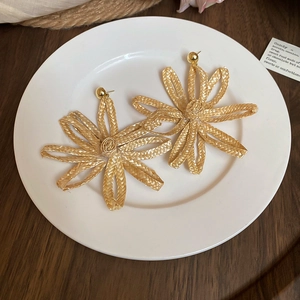 Detail view of bohemian flower earrings made of woven raffia material on a white plate