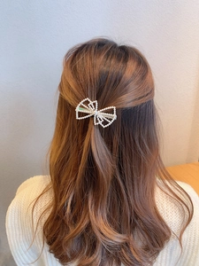 Detailed view of pearl bow hair clip styled on a woman's wavy brown hair for a chic look