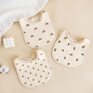 Three-piece baby cotton gauze bibs with rainbow, lemon, and heart prints on warm background
