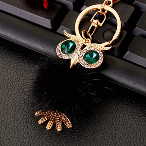 Detailed macro view of owl keychain with green crystal eyes and fluffy black fur pompom