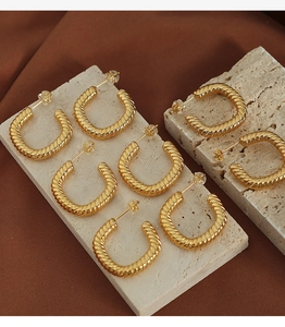 Detail shot of golden twisted rope earrings on stone display with silk background