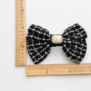 Detail shot of a black and white plaid woven bow hair clip with a large central pearl