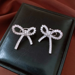 Detailed view of silver bow-shaped clip earrings with sparkling cubic zirconia on dark fabric