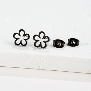 Macro shot of minimalist black hollow flower earrings on white stone surface