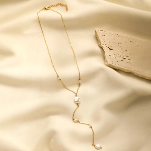 Detail view of gold-plated Y-shaped pearl tassel necklace on beige textured fabric