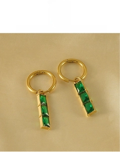 Gros plan détaillé de boucles d'oreilles en acier doré 18K avec trois pierres vert émeraude