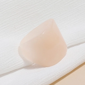 Close-up of translucent pink resin ring on white pleated fabric with minimal lighting