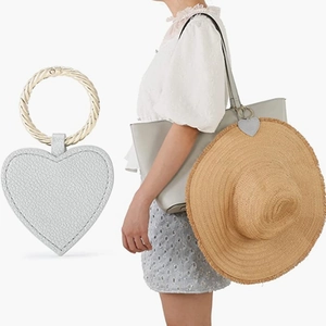 Detail of grey heart-shaped leather hat clip with gold ring shown on a bag