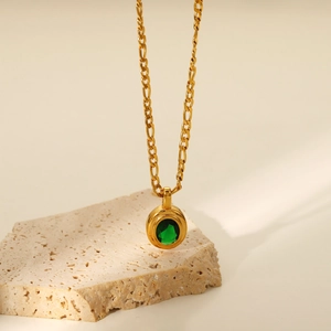 Close-up of a gold necklace with a green oval gemstone pendant over a stone