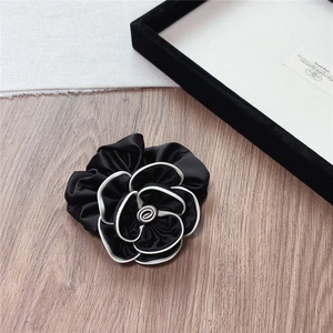 Detail of satin camellia flower hair scrunchie with contrast white edge on wood background