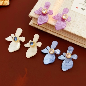 Gros plan de boucles d'oreilles fleurs en résine avec base dorée et zircon en trois couleurs