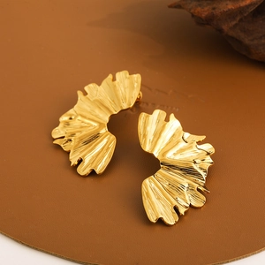 Macro view of golden ginkgo leaf earrings with detailed texture on brown leather