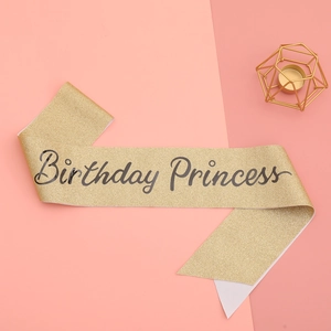 Close-up of glitter gold Birthday Princess sash with black calligraphy on pink background