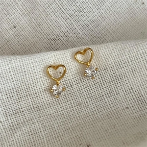 Detailed view of heart-shaped gold studs with clear zircon drops on white fabric