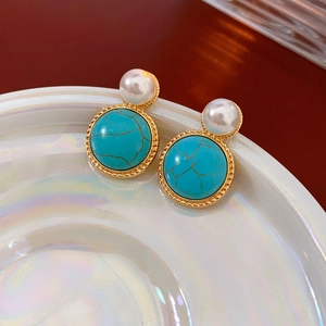 Close-up of vintage gold rimmed turquoise earrings with white pearl detail on white dish