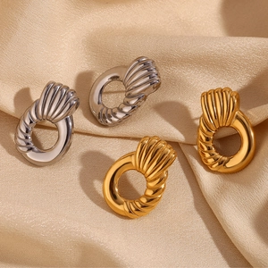 Twisted geometric hoop earrings in gold and silver finish on silk fabric background