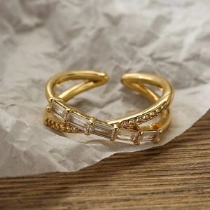 Crossed double band 18K gold plated ring with emerald-cut zircon stones on a wooden surface