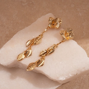 Macro shot of gold metallic leaf fringe earrings resting on a textured light stone base