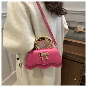 Detail of pink crossbody bag with wavy edge, golden metal bow and metallic top handle