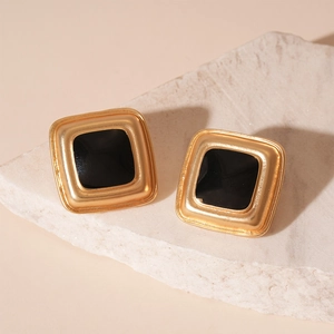 Macro detail of square gold earrings with black enamel inlay on natural stone background