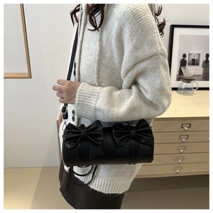 Détail d'un sac cylindrique noir à nœuds porté par un mannequin dans un intérieur