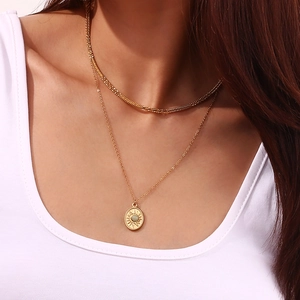 Detail showing a 18K gold layered snake chain and sun pendant with a green gemstone