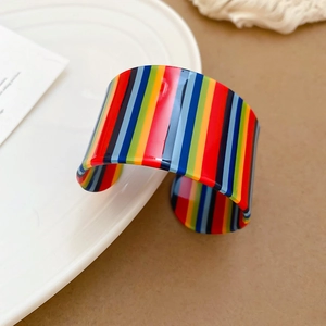Detailed view of a wide C-shaped acrylic bangle with vibrant vertical rainbow stripes