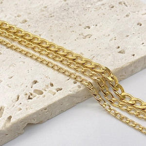 Three gold stainless steel Cuban link chains in different widths on beige stone background