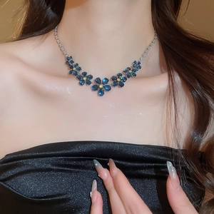 Close-up of deep blue zircon flower pendant necklace on collarbone with silver chain