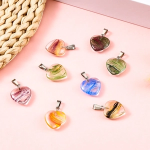 Flat lay of colorful Millefiori heart-shaped glass pendants with silver bails on pink background