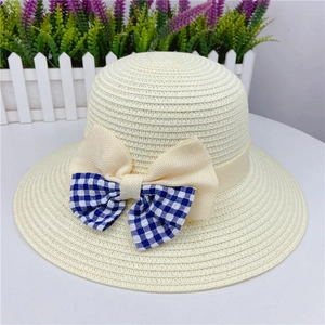 Detail of straw sun hat featuring a blue plaid and beige layered ribbon bow accent