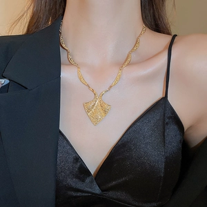 Close-up of golden geometric fan pendant on a flat snake chain worn by a model