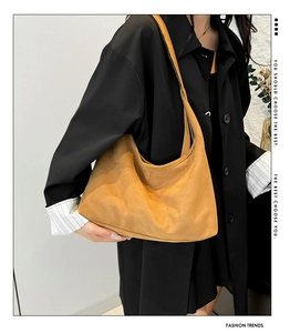 Detail view of a vintage brown matte suede hobo bag carried by a model in a black jacket
