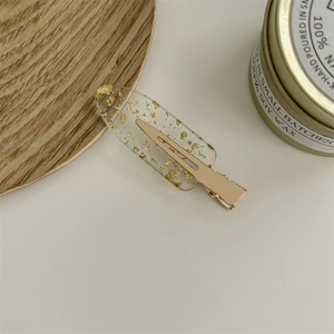 Close-up of a clear hair clip with gold foil flakes and a durable golden metal base