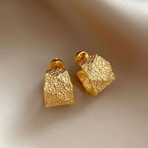 Macro shot of gold-plated geometric C-shape earrings with irregular crinkle texture