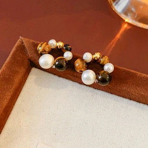 Detailed macro shot of vintage pearl and tiger eye earrings on a premium display stand