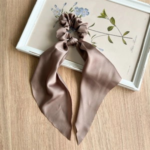 Detailed view of champagne satin scrunchie with elegant ribbons on a decorative frame