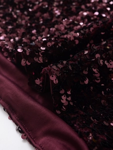 Macro shot of dark burgundy sequins on an elegant dress with shimmering light reflections