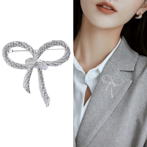 Macro detail of silver bow brooch with woven texture pinned on a grey suit blazer