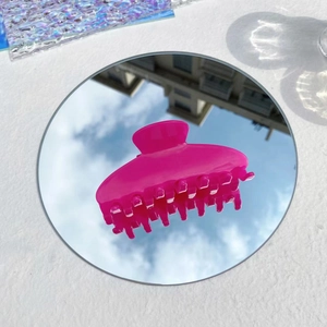 Close-up of pink acetate hair claw clip reflecting clear sky and clouds on a mirror