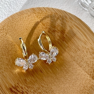 Macro shot of gold butterfly earrings with sparkling cubic zirconia on a wooden tray