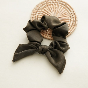 Close-up of a dark green bow scrunchie with fine fabric texture on a woven coaster
